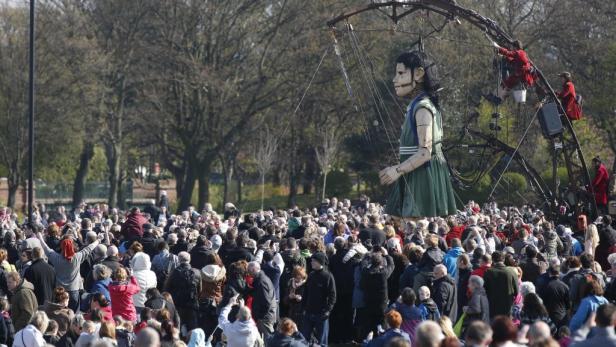 Eine riesige Marionette steht inmitten einer Menschenmenge in einem Park.