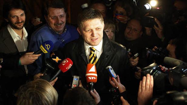 Robert Fico wird von Reportern und Mikrofonen umringt.