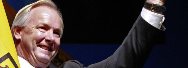 Ein lächelnder Mann im Anzug hebt den Arm.