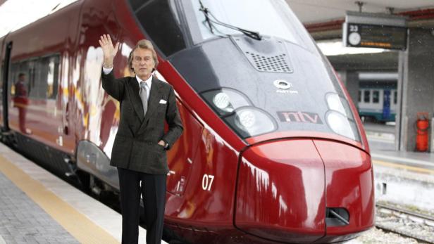 Ein Mann im Anzug steht vor einem roten Hochgeschwindigkeitszug und winkt.
