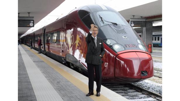 Ein Mann in einem Anzug steht vor einem roten Hochgeschwindigkeitszug auf einem Bahnsteig.