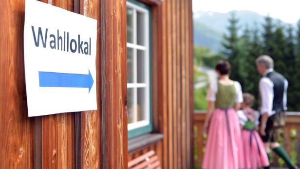 Ein Schild mit der Aufschrift „Wahllokal“ und ein Familie in Tracht vor einem Wahllokal.