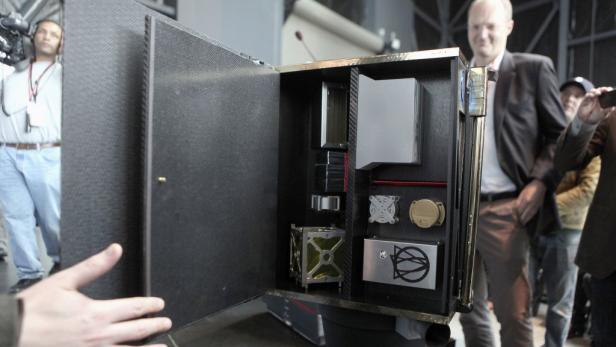 Ein geöffneter Koffer mit verschiedenen technischen Geräten und einem kleinen Satellitenwürfel darin.
