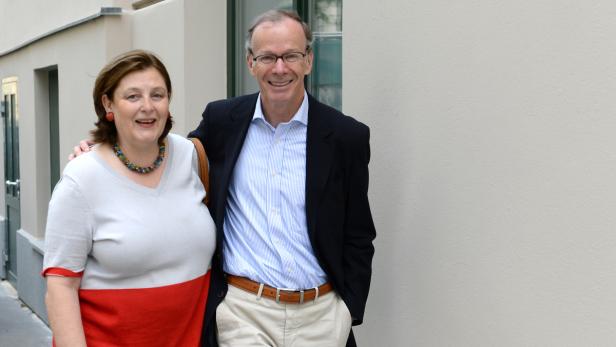 Ein Mann mit Brille und eine Frau stehen lächelnd vor einer hellen Wand.