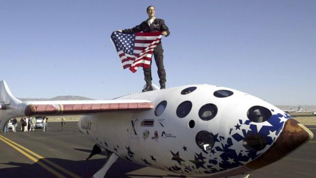 Ein Mann steht mit einer US-Flagge auf dem SpaceShipOne-Raumflugzeug.