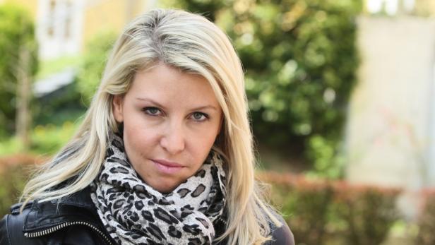 Eine blonde Frau mit einem Schal mit Tiermuster blickt in die Kamera.
