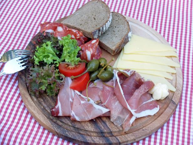 Eine Brotzeitplatte mit Wurst, Käse, Schinken und Gemüse auf einem Holzteller.