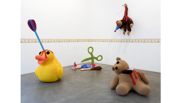 Eine Szene mit Stofftieren, die Gewalt darstellen, darunter eine Ente mit einem Pfeil im Kopf und ein Teddybär mit einer Schere im Hals.