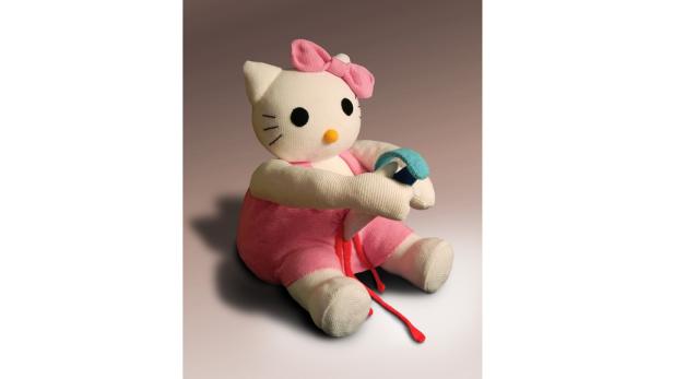 Eine gehäkelte Hello Kitty-Puppe mit rosa Schleife und Latzhose hält ein blaues Armband.