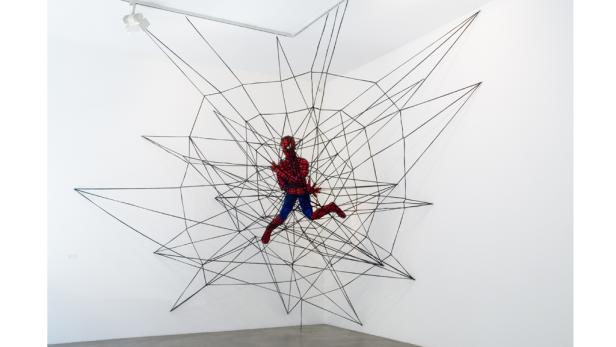 Eine Spiderman-Figur hängt in einem Netz aus schwarzen Linien an einer weißen Wand.