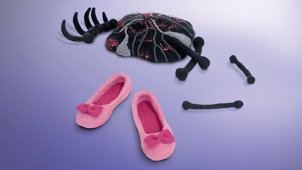 Gehäkelte rosa Ballettschuhe und eine Spinne mit Knochen liegen auf einem lila Hintergrund.
