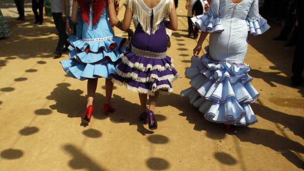 Drei Frauen in farbenfrohen Flamenco-Kleidern gehen auf einer Straße.