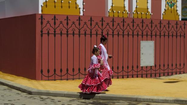 Zwei Mädchen in traditionellen Flamenco-Kleidern gehen an einem Gebäude vorbei.
