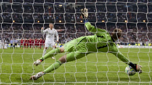 Ein Torwart in grüner Uniform springt, um einen Ball zu halten, während Cristiano Ronaldo im Hintergrund jubelt.