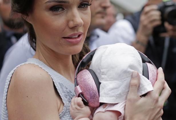 Eine Frau hält ein Baby mit rosafarbenen Kopfhörern, vermutlich zum Schutz vor Lärm.