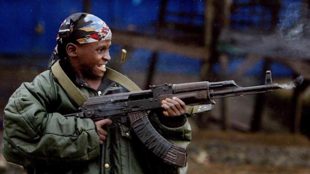 Ein junger Mann mit einem Tuch auf dem Kopf schießt mit einem AK-47 Gewehr.