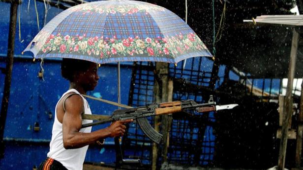 Ein Mann mit einem Gewehr steht im Regen unter einem Regenschirm.