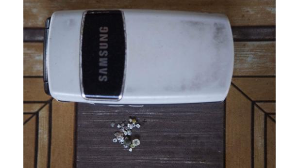 Ein altes Samsung-Klapphandy liegt neben einer kleinen Ansammlung von Rohdiamanten.