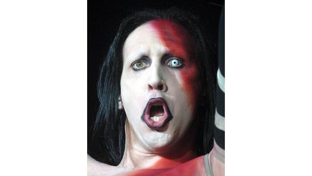 Marilyn Manson mit weiß geschminktem Gesicht und unterschiedlichen Kontaktlinsen, den Mund geöffnet.