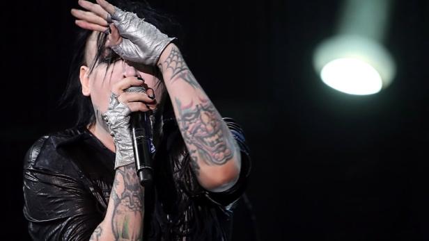 Marilyn Manson singt mit tätowierten Armen in ein Mikrofon.