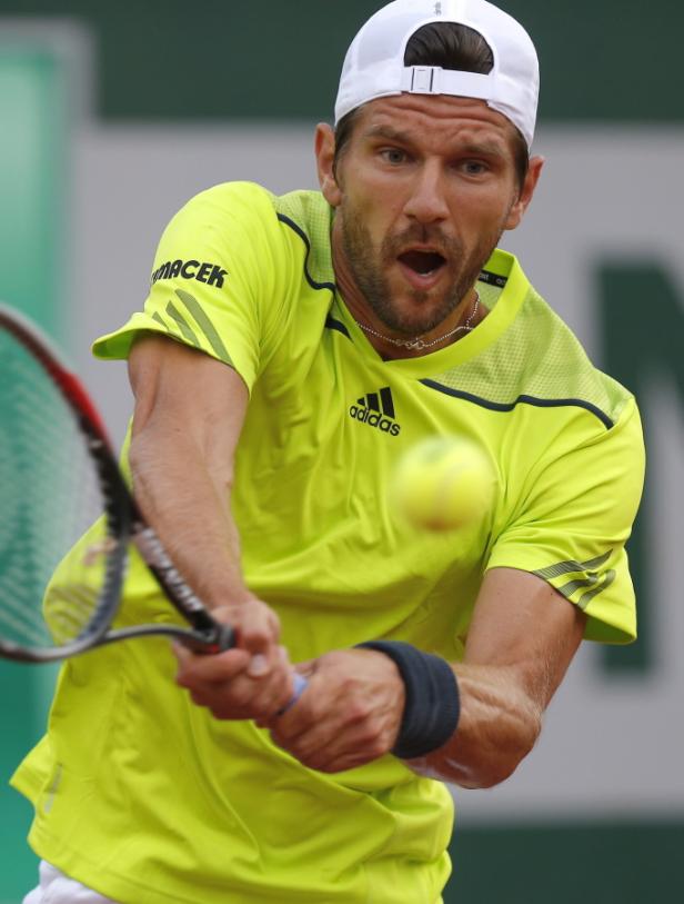 Ein Tennisspieler in einem gelben Hemd schlägt einen Ball.