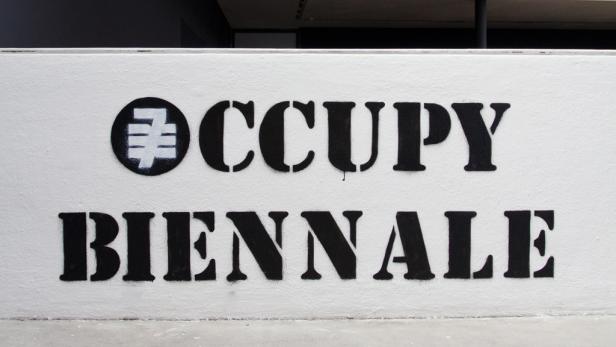 Auf einer Wand steht in schwarzer Schrift „Occupy Biennale“.