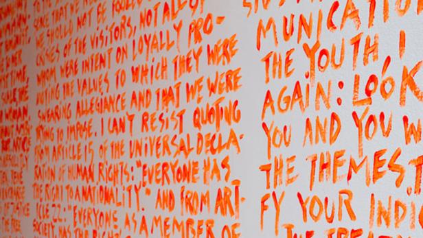 Eine Wand mit orangefarbener Schrift, die Zitate und Sätze über Jugend und Rechte enthält.