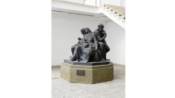 Eine Skulptur einer sitzenden Frau mit Kind, flankiert von zwei Männern.