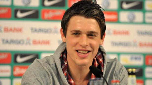 Ein junger Mann lächelt vor einer Wand mit Logos von Banken und Nike.