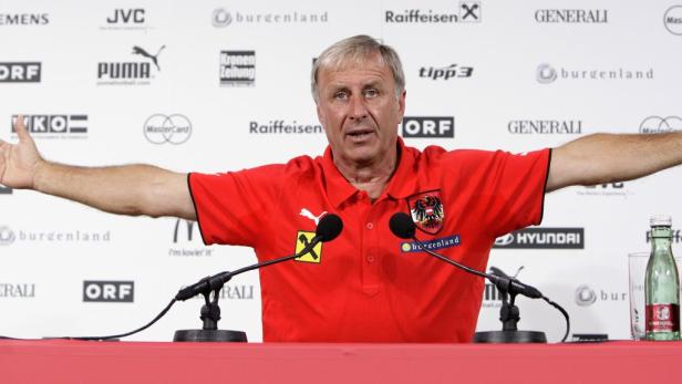 Ein Mann im roten Poloshirt mit dem österreichischen Wappen steht vor einer Wand mit Sponsorenlogos.