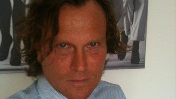 Ein Mann mit braunen Haaren und einem hellblauen Hemd blickt in die Kamera.