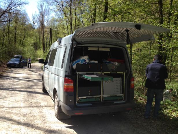 Ein Polizei-Van mit geöffneter Heckklappe steht auf einem Waldweg.