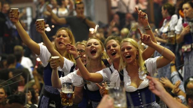 Frauen in Dirndln feiern mit Bierkrügen auf dem Oktoberfest.