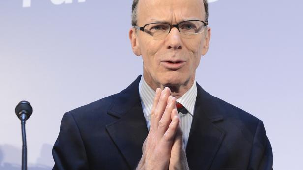 Ein Mann mit Brille und Anzug steht vor einem Mikrofon und spricht.