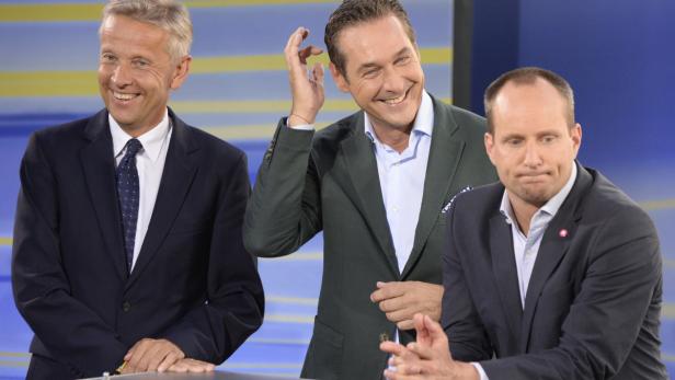 Drei Männer in Anzügen stehen oder sitzen vor einem blauen Hintergrund.