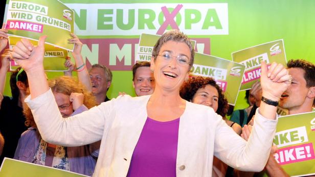 Eine lächelnde Politikerin der Grünen gibt vor einem Wahlkampf-Hintergrund beide Daumen nach oben.