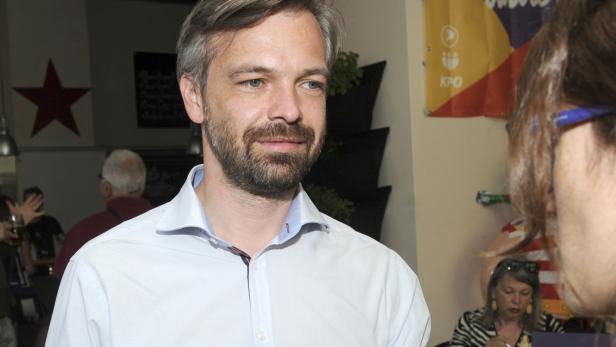 Ein Mann mit Bart und hellblauem Hemd steht in einem Raum mit einer roten Stern-Dekoration.