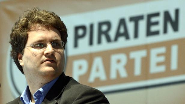 Ein Mann mit Brille steht vor einem Schild der Piratenpartei.
