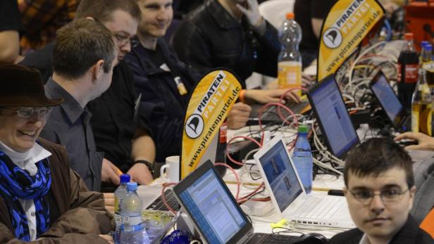Menschen sitzen an Tischen mit Laptops und einem Banner der Piratenpartei.