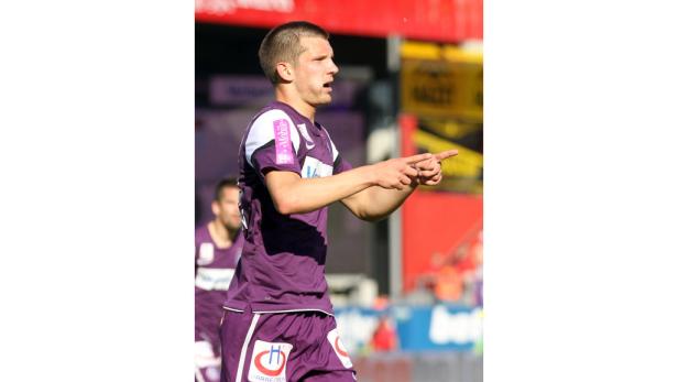 Ein Fußballspieler in lila Sportkleidung zeigt mit dem Finger zur Seite.
