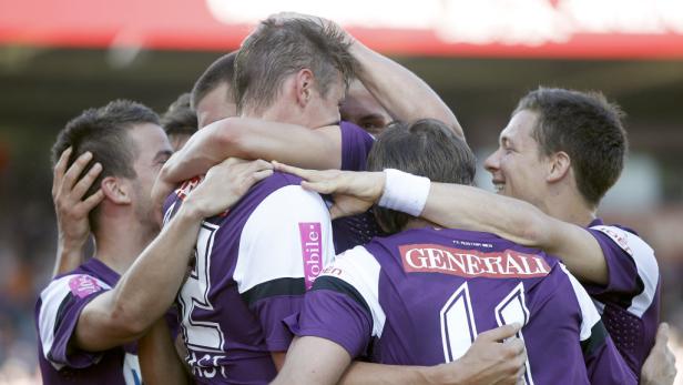 Eine Gruppe Fußballspieler in lila Trikots umarmt sich jubelnd.