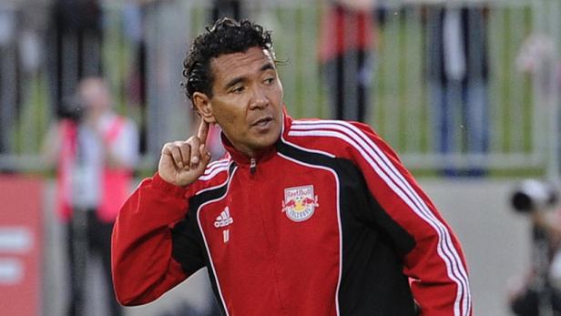 Ein Mann in einer roten Jacke mit dem Red Bull Logo deutet mit dem Finger an seine Schläfe.