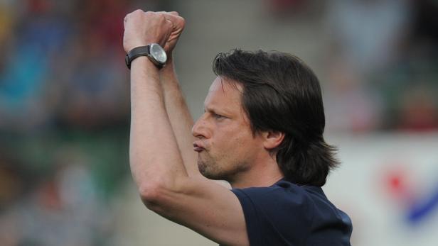 Ein Mann mit dunklen Haaren und einer Armbanduhr jubelt mit erhobenen Fäusten.