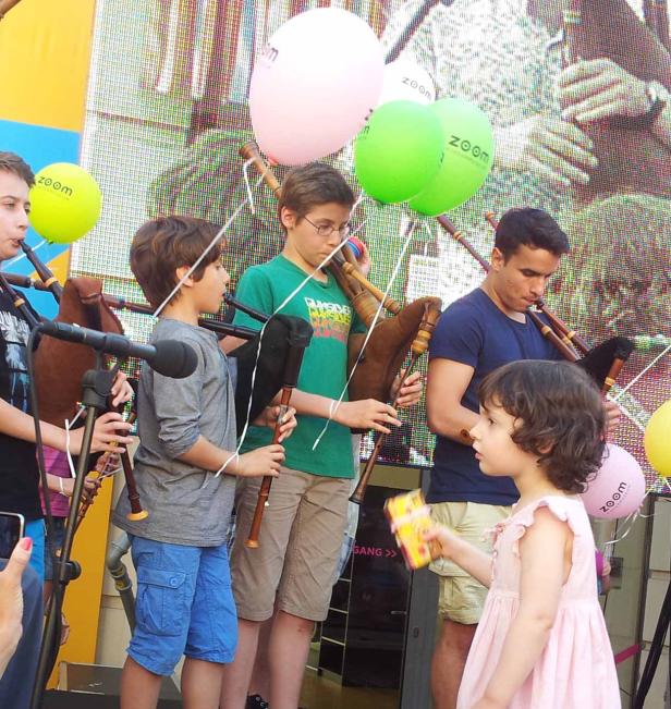 Eine Gruppe von Jungen spielt Dudelsack, während ein kleines Mädchen zusieht.