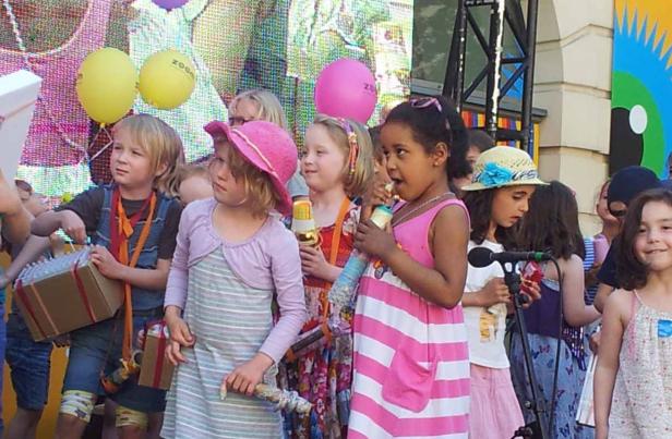 Eine Gruppe Kinder steht auf einer Bühne mit Ballons und bunten Dekorationen.