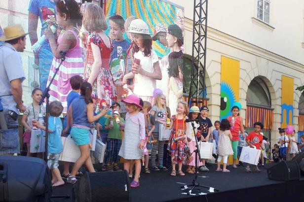 Eine Gruppe Kinder steht auf einer Bühne vor einer großen Leinwand.