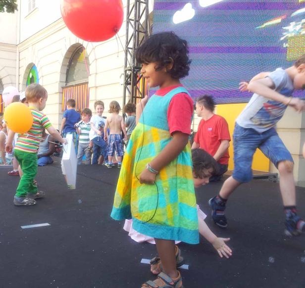 Eine Gruppe Kinder spielt auf einer Bühne mit bunten Luftballons.