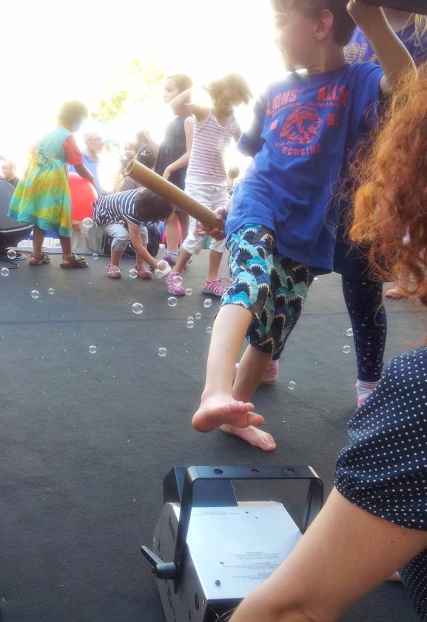Kinder spielen mit Seifenblasen auf einer Bühne.