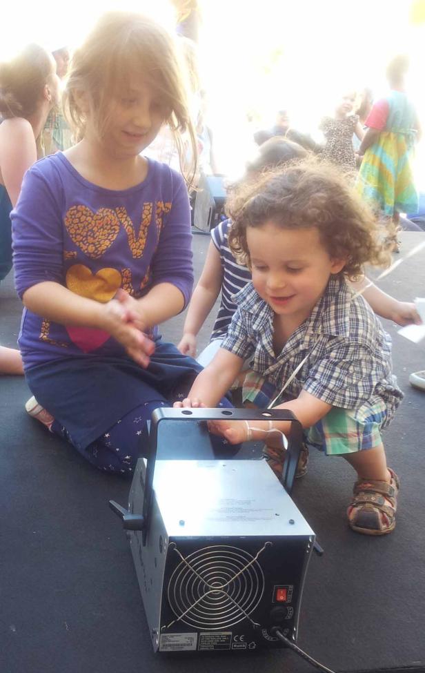 Zwei Kinder spielen mit einer Nebelmaschine auf einer Bühne.