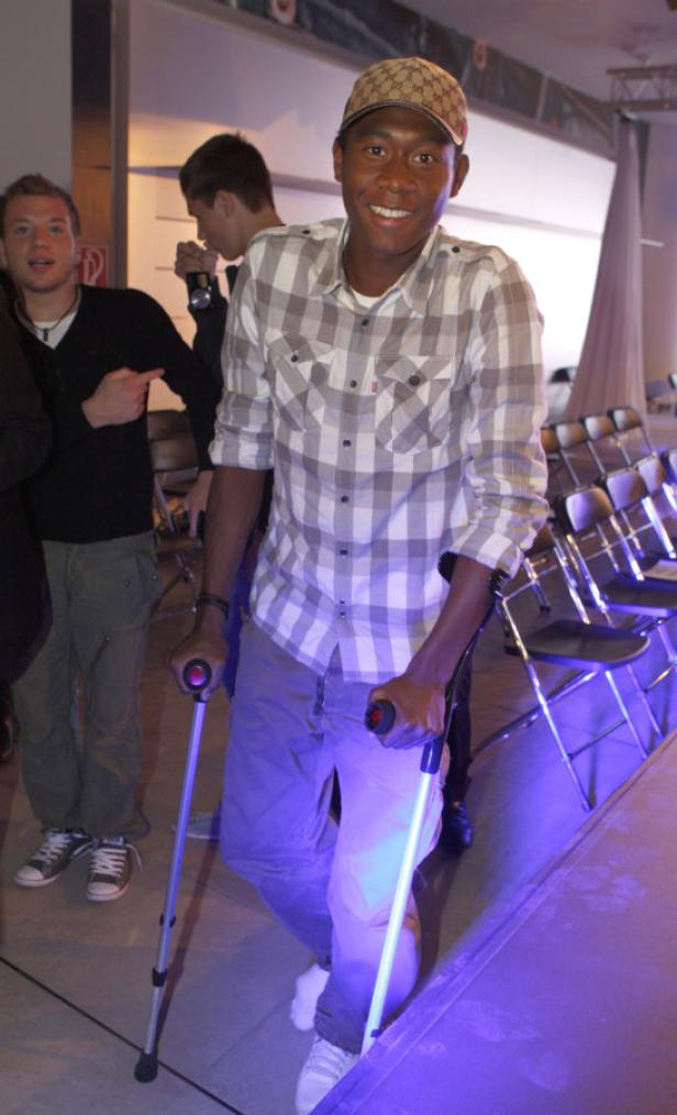 Ein lächelnder Mann mit Krücken und einer Kappe steht auf einer Bühne.